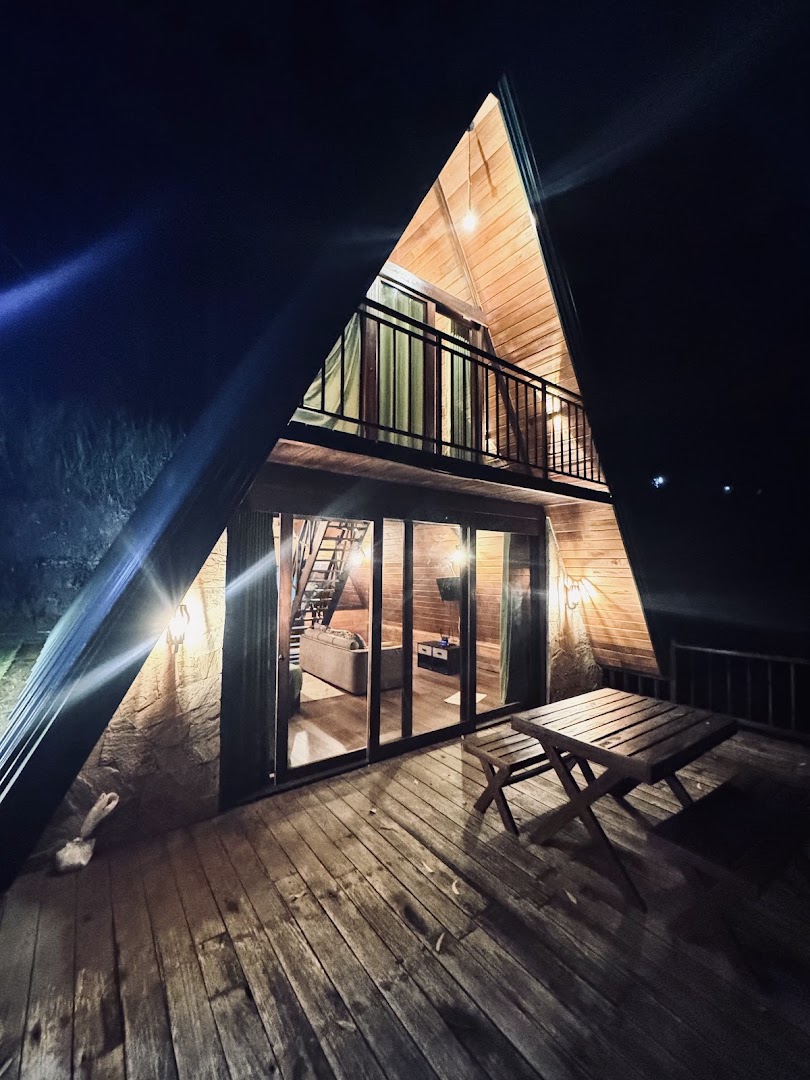 A-frame wooden cabana lit warmly at night with a deck and balcony