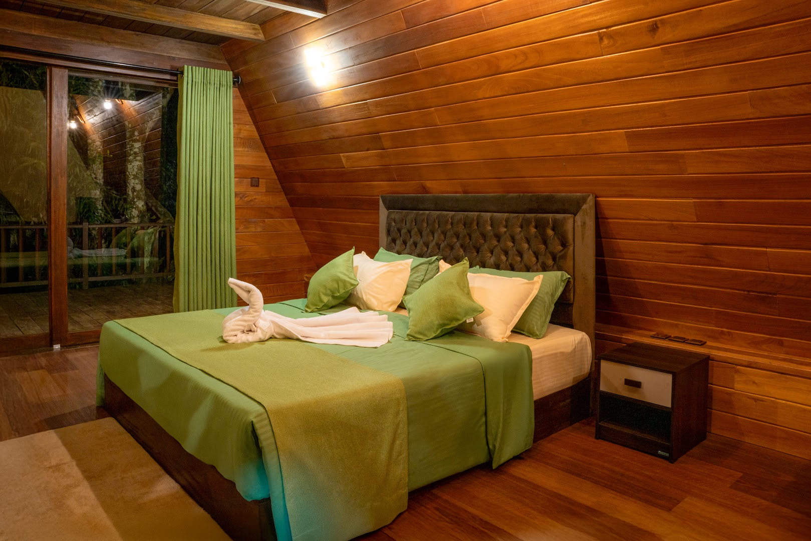 Warm timber bedroom with olive green bedding and a glass door opening to trees