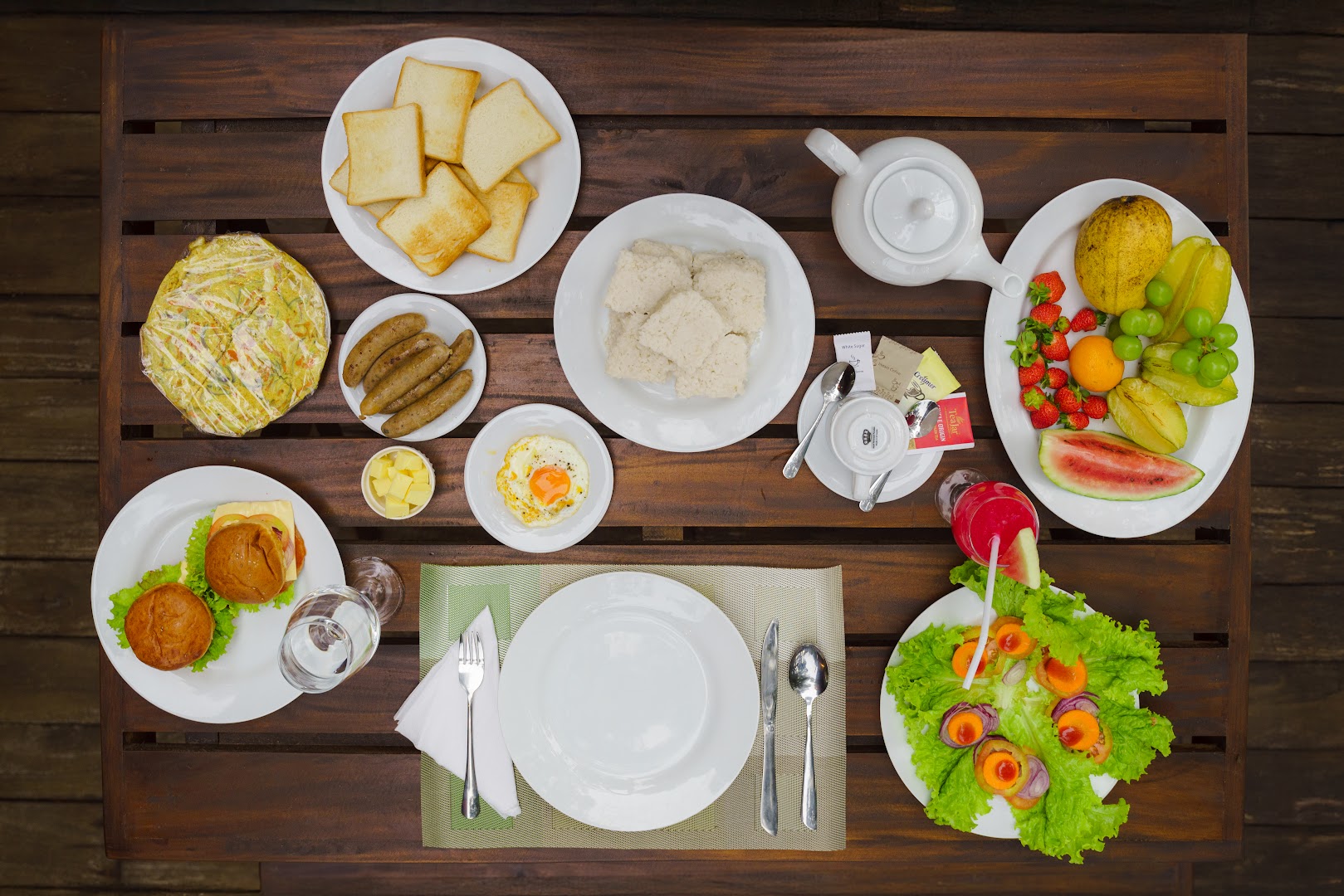 Breakfast spread with fruit, toast, eggs, tea, and other dishes on a timber table